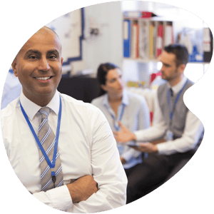 man in dress shirt looking at the camera with teachers having a discussion in the background
